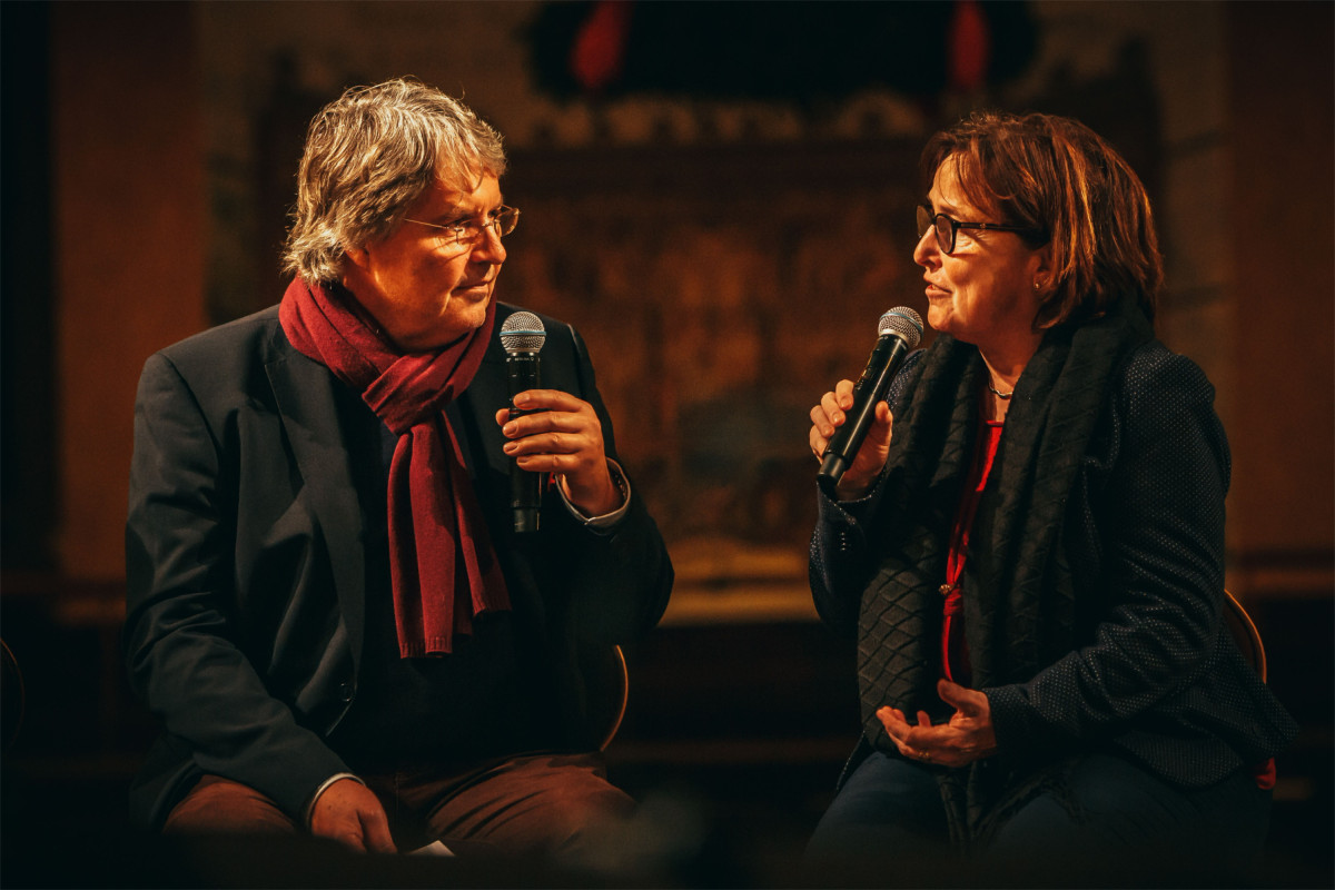 Zwei Personen führen ein Bühnengespräch mit Mikrofonen vor Publikum.