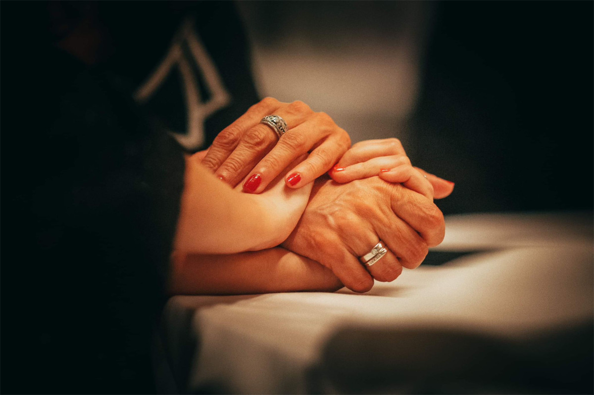 Zwei Personen halten sich an den Händen, Nahaufnahme mit warmem Licht.