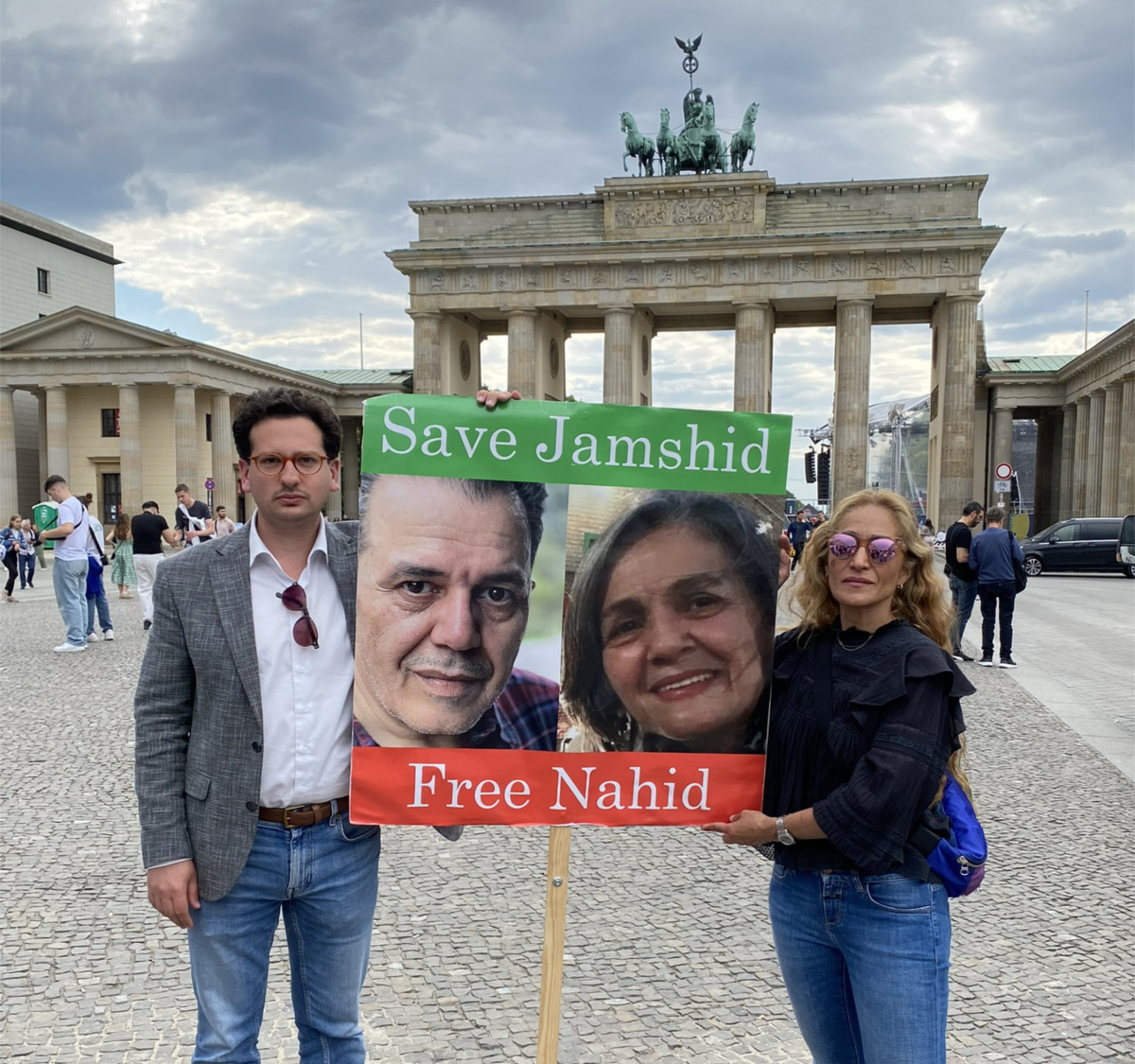 Bastian Mahmoodi steht mit einer Frau vor dem Brandenburger Tor und hält ein Plakat mit der Aufschrift „Save Jamshid, Free Nahid“.