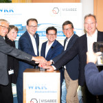 Bastian Mahmoodi steht mit fünf weiteren Personen beim offiziellen Start eines Projekts von VISABEE und den Westküstenkliniken.